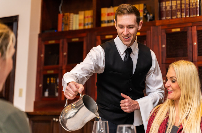 a server pouring water into a glass for a table of restaurant goers