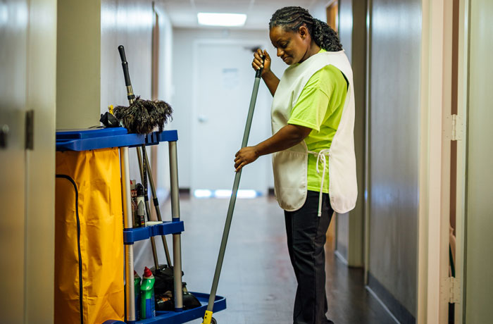 Janitorial staff using a vacuum to clean a rug near a door